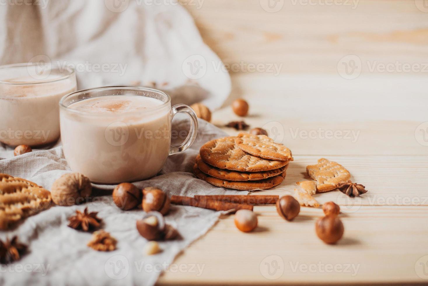 Hot cocoa with cookies, cinnamon sticks, anise, nuts on wooden background. photo