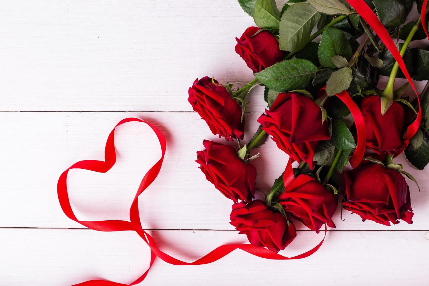 Red ribbon shaped as heart, bouquet of roses and gift boxes wrapped in kraft papper on white wooden table. photo