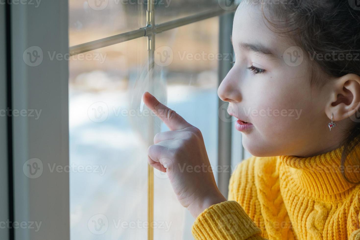 A girl in a yellow sweater looks out the window. Childhood dreams, a look into the future. Copy space photo