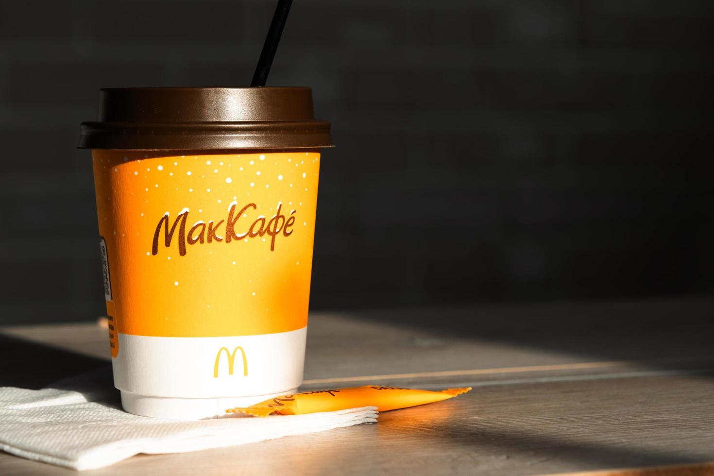 Coffee to go of McDonald's with the inscription Maccafe in Russian stick with sugar on the table with a napkin and a straw. Fast food restaurant chains. Russia, Kaluga, March 21, 2022. photo