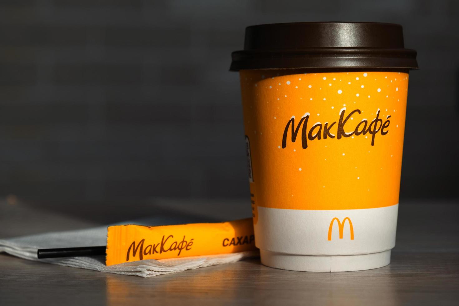 Coffee to go of McDonald's with the inscription Maccafe in Russian stick with sugar on the table with a napkin and a straw. Fast food restaurant chains. Russia, Kaluga, March 21, 2022. photo