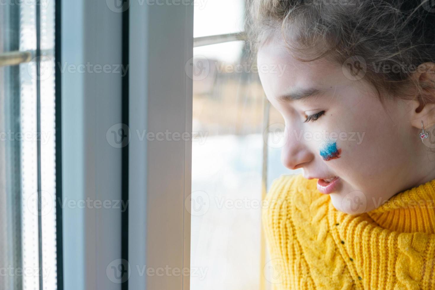 un niño triste en la ventana con la bandera de rusia, se preocupa con lágrimas en los ojos. conflicto entre rusia y ucrania, miedo foto