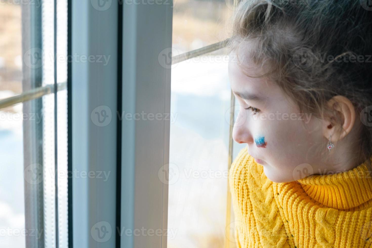un niño triste en la ventana con la bandera de rusia, se preocupa con lágrimas en los ojos. conflicto entre rusia y ucrania, miedo foto