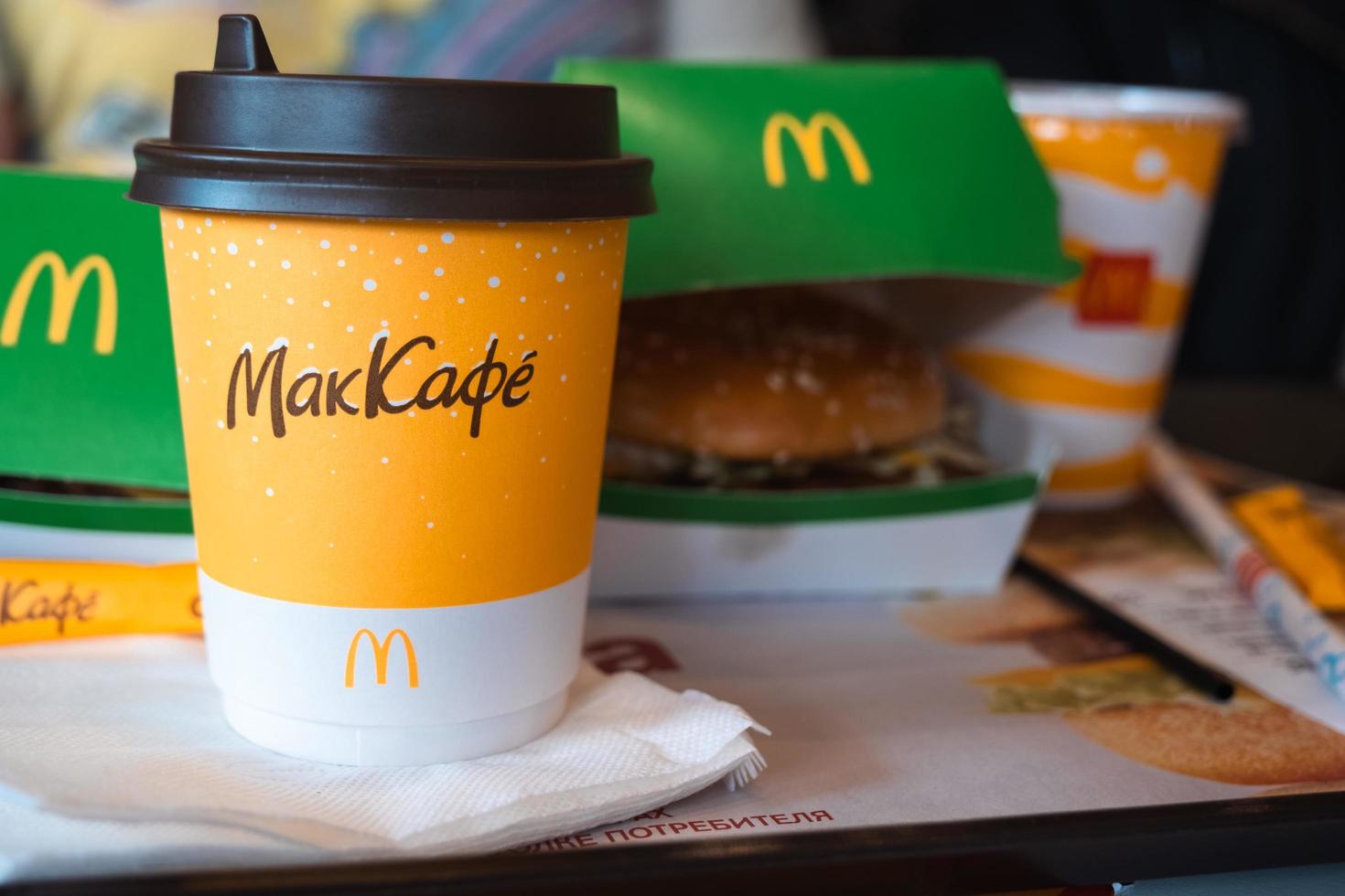 A paper cup of McDonald's coffee with the inscription Maccafe in Russian and a hamburger in a box on a tray. Fast food restaurant chains. Russia, Kaluga, March 21, 2022. photo