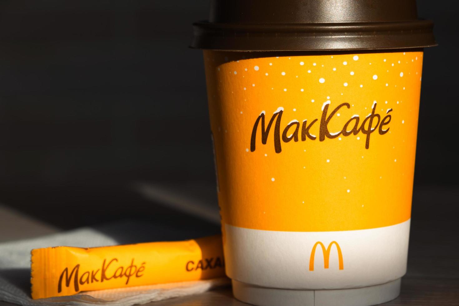 Coffee to go of McDonald's with the inscription Maccafe in Russian stick with sugar on the table with a napkin and a straw. Fast food restaurant chains. Russia, Kaluga, March 21, 2022. photo