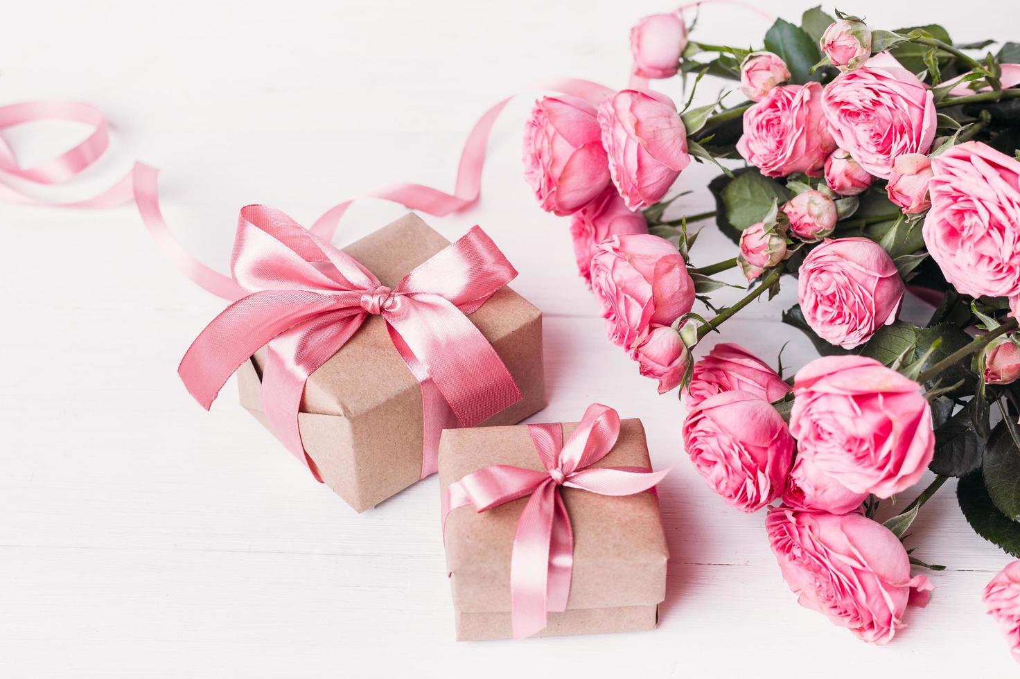 Fresh pastel soft pink roses, and gift boxes wrapped in kraft papper with ribbons on white wooden table. photo