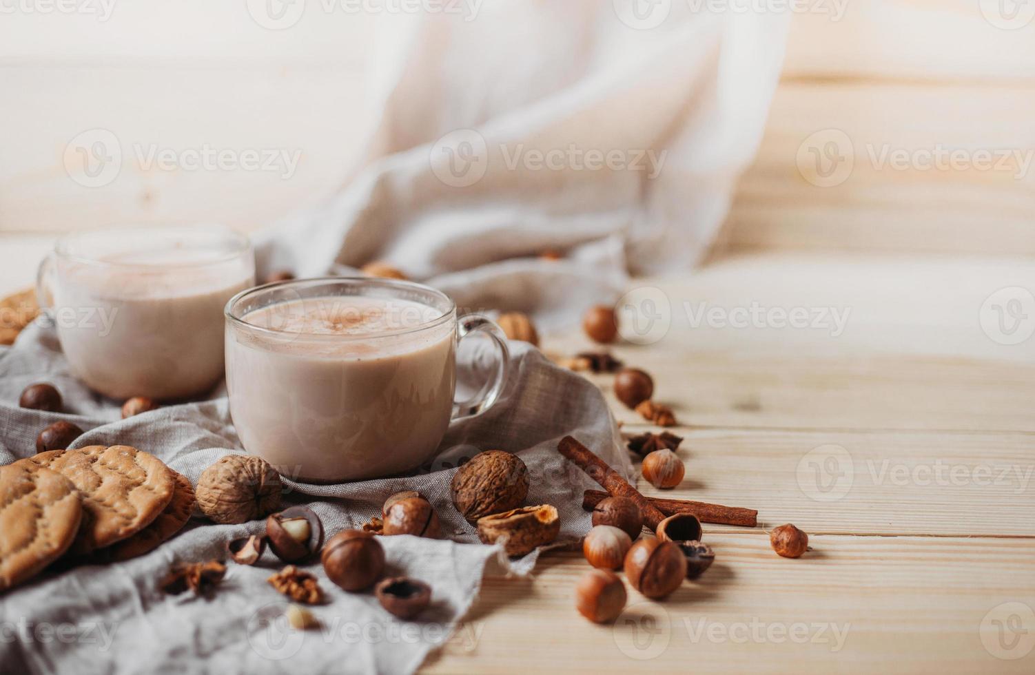 Hot cocoa with cookies, cinnamon sticks, anise, nuts on wooden background. photo