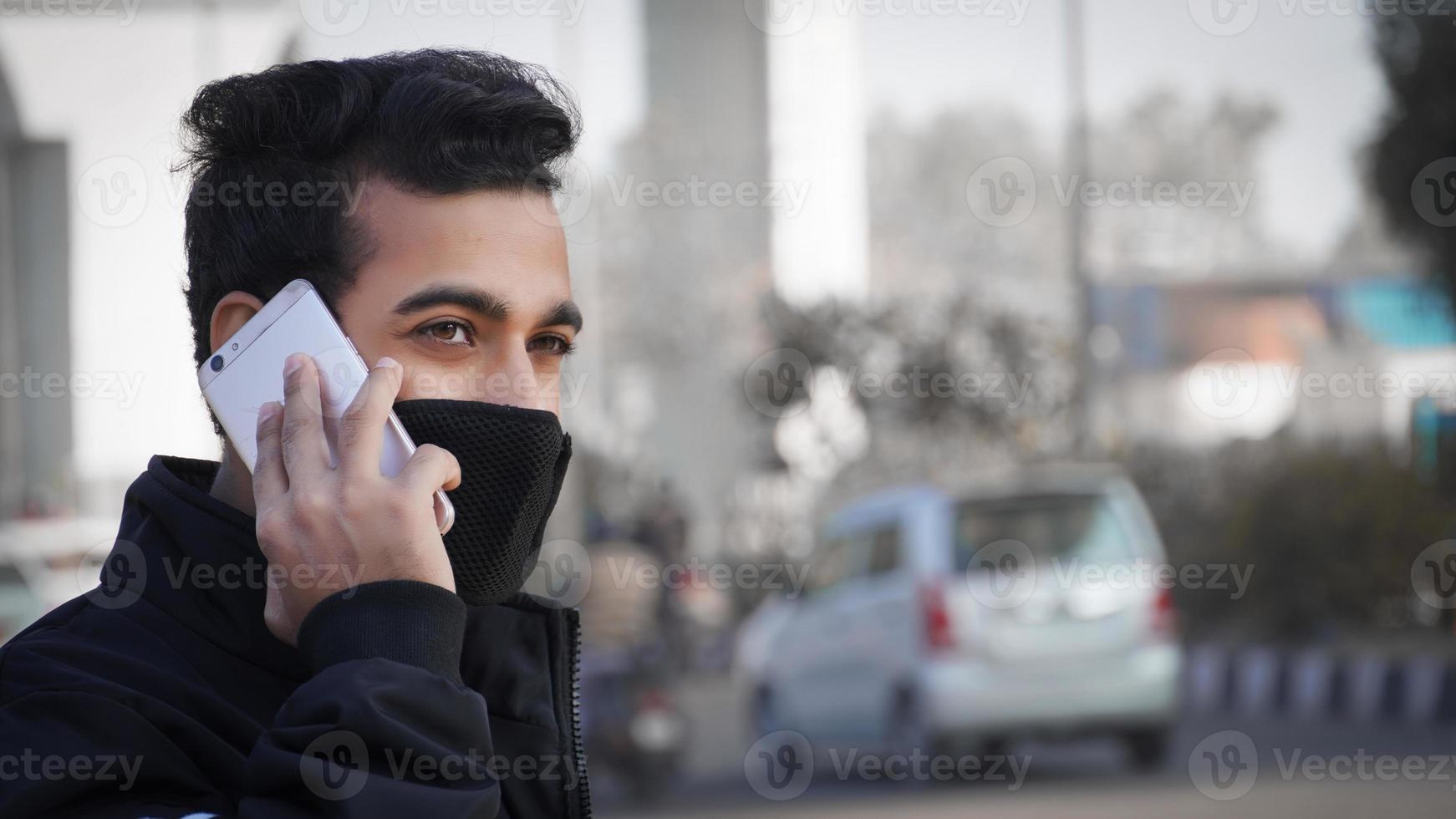 Young man holding mobile phone, using smartphone, making a call, talking on the phone, standing on street with transport traffic on the background photo