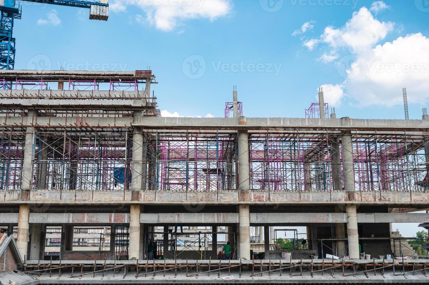 Structure of large building with worker working, crane and scaffold in construction site photo