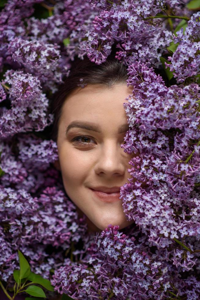 A pregnant beautiful woman lies on her side in a purple bodysuit. Lilac is strewn around her everywhere. Place for a logo. photo