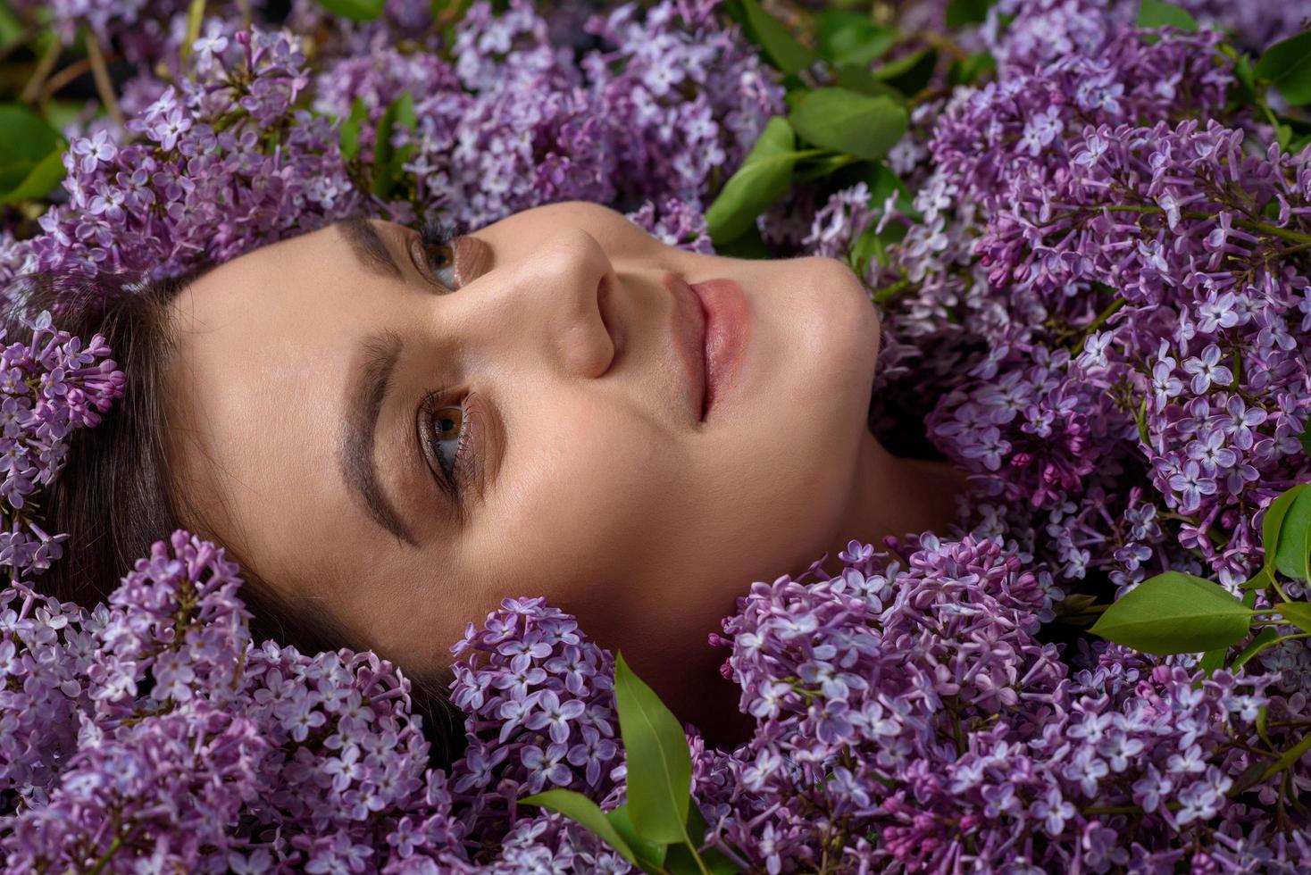 una hermosa mujer embarazada yace de lado con un traje morado. la lila está esparcida a su alrededor por todas partes. lugar para un logotipo. foto