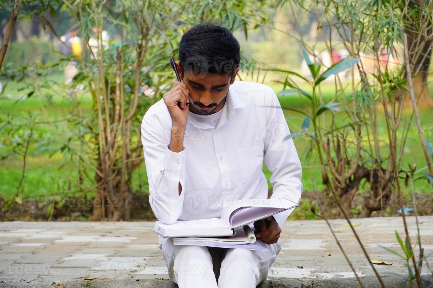 Indian student reading book near college campus photo