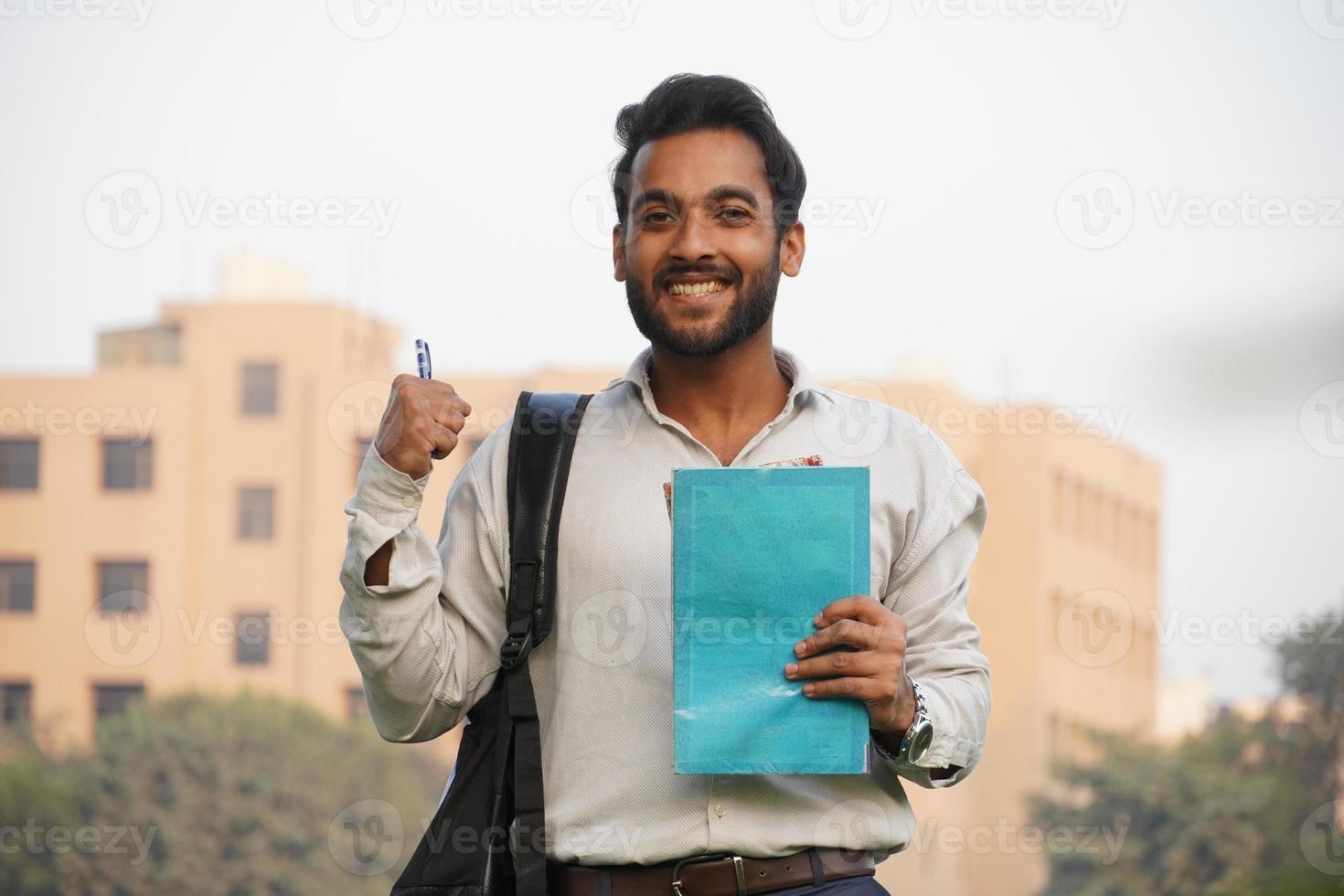 joven estudiante universitario con libros y pluma y de pie sobre el edificio del collage foto