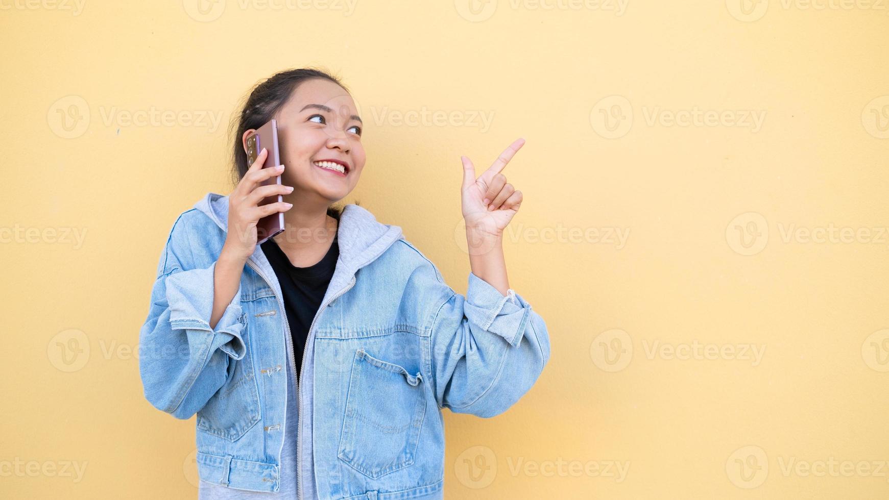 retrato hermosa joven usa chaqueta jean hablando con móvil en bcakground naranja, chica asiática. foto