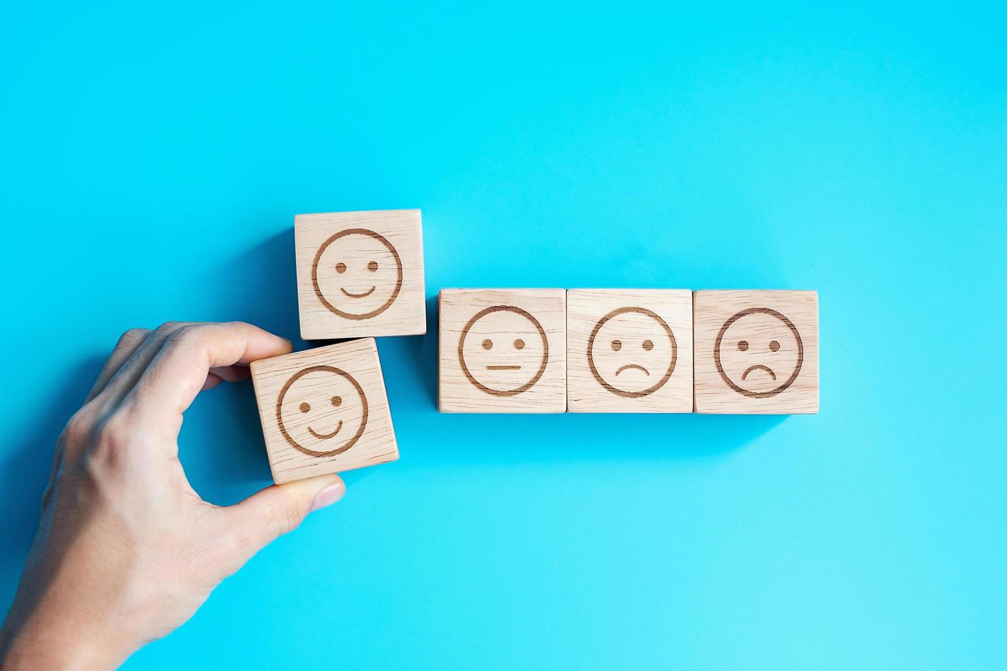 Man hand holding emotion face block. Customer choose Emoticon for user reviews. Service rating, ranking, customer review, satisfaction, evaluation and feedback concept photo