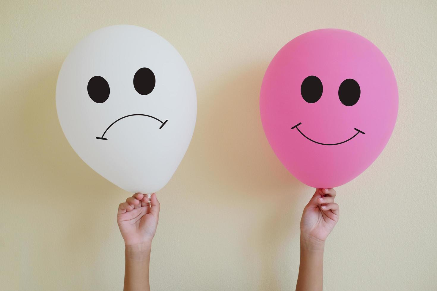 Close up hand's kid holding the smiling face pink balloon and sadly face pink balloons on yellow wall background. Realistic balloon. Thinking concepts. Emotional concept. photo