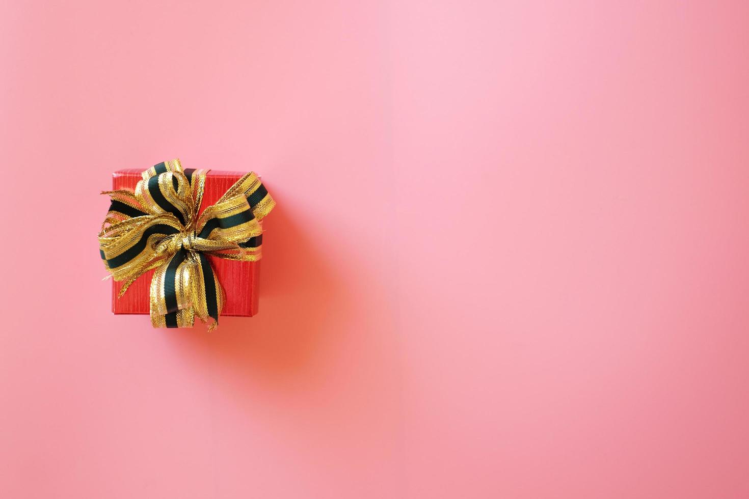 Red gift box with ribbon isolated on pink background for giving in holidays with copy space for text. Holidays, present, giving concept. New year day, Christmas day, Chinese New Year day, Birthday. photo