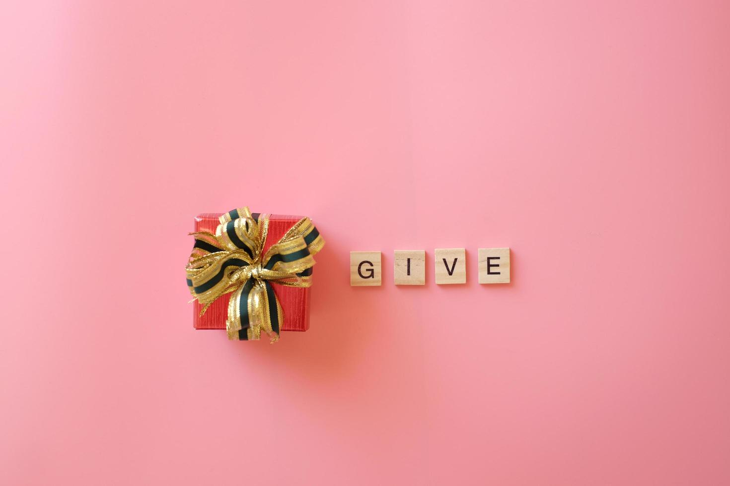 Red gift box with ribbon isolated on pink background for giving in holidays with wooden letters  give. Holidays, present, giving concept. New year day, Christmas day, Chinese New Year day, Birthday. photo