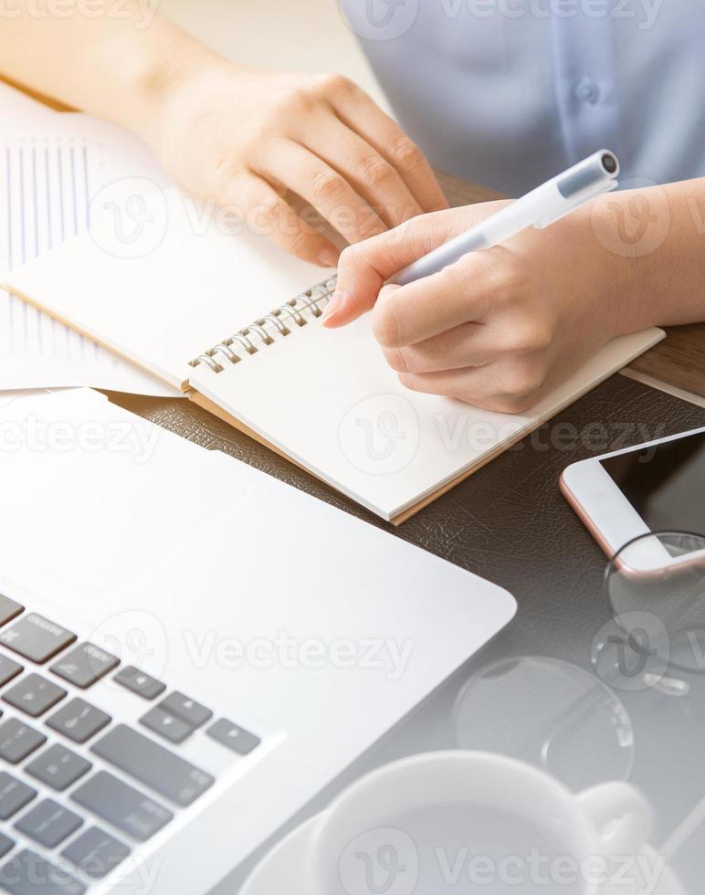 Business concept. Woman takes note for project with laptop and report in office desk. Backlighting, sun glare effect, close up, side view, copy space photo