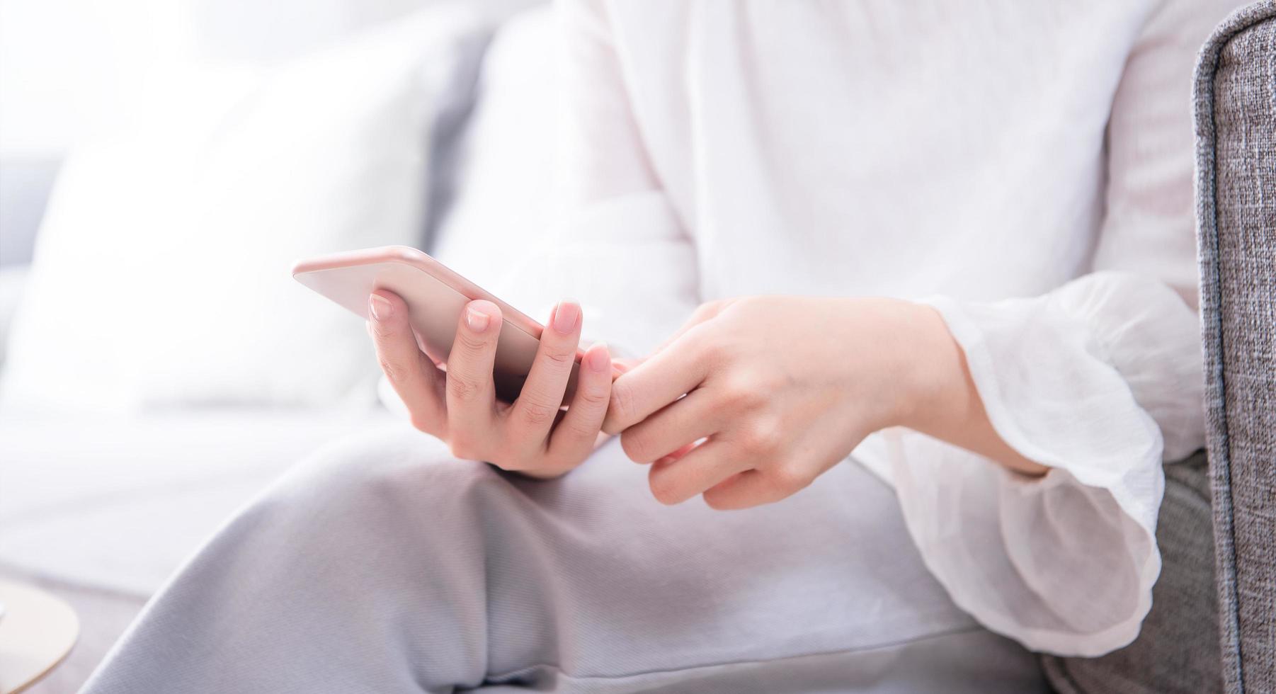 Side view of asia young woman in white sitting on sofa and using smart phone in bright living room, copy space, close up, blank for design concept photo