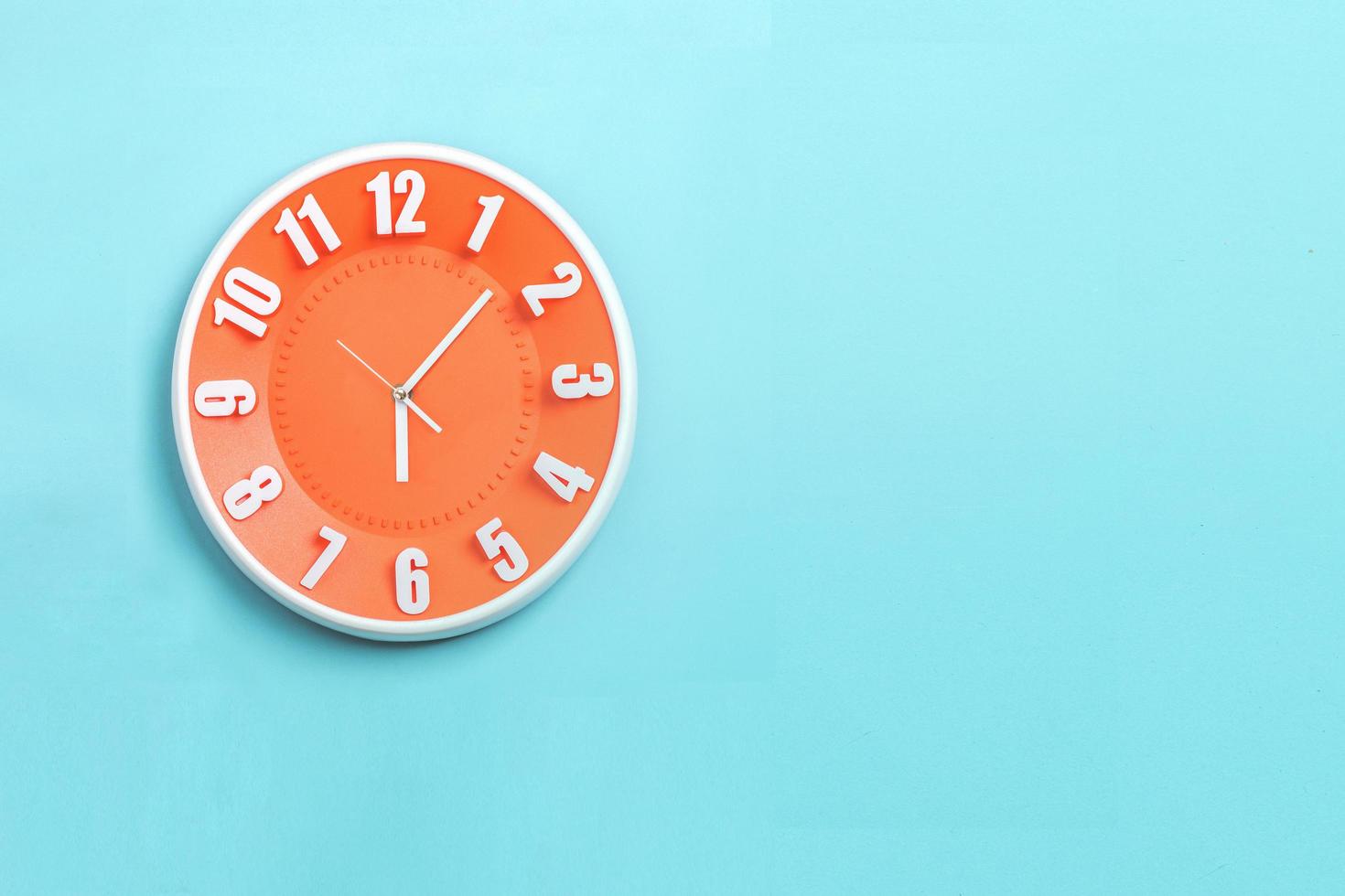 hermoso reloj de pared naranja sobre fondo azul, concepto de empezar la mañana a trabajar. foto