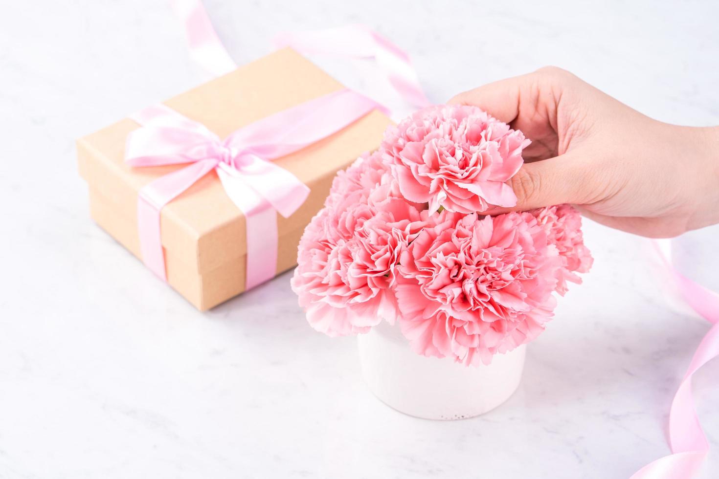 Design concept - Woman giving carnations bouquet on marble white background, top view, copy space, close up, mock up. Mothers day idea inspiration. photo