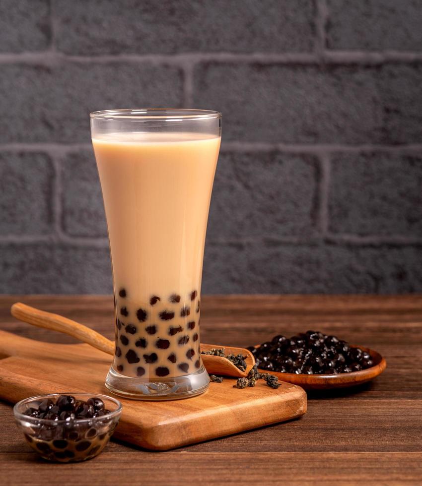 delicioso té de leche con burbujas con bola de perlas de tapioca en vidrio sobre mesa de madera y fondo de ladrillo gris oscuro, comida y bebida popular en taiwán, cerrar foto