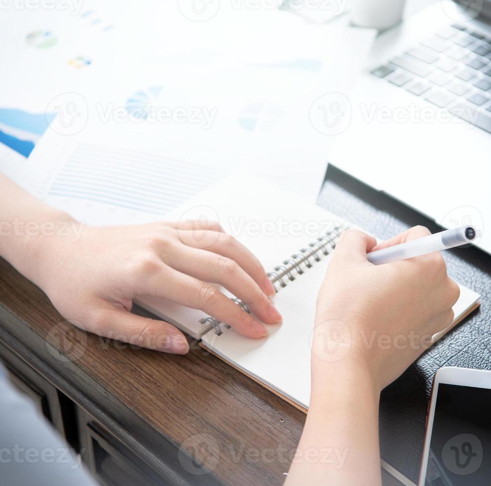 Business concept. Woman takes note for project with laptop and report in office desk
