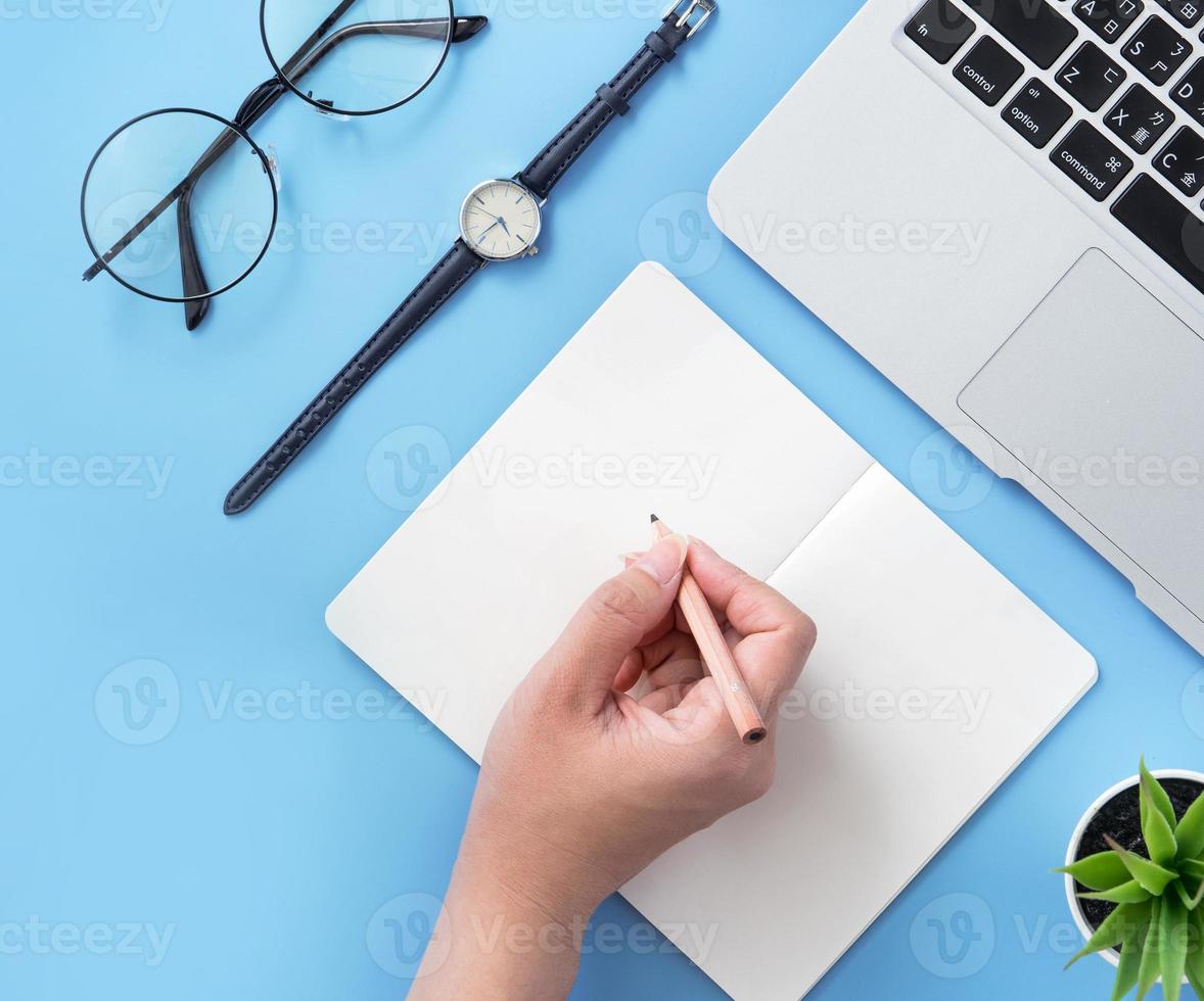 Girl write on open white book or accounting on a minimal clean light blue desk with laptop and accessories, copy space, flat lay, top view, mock up photo