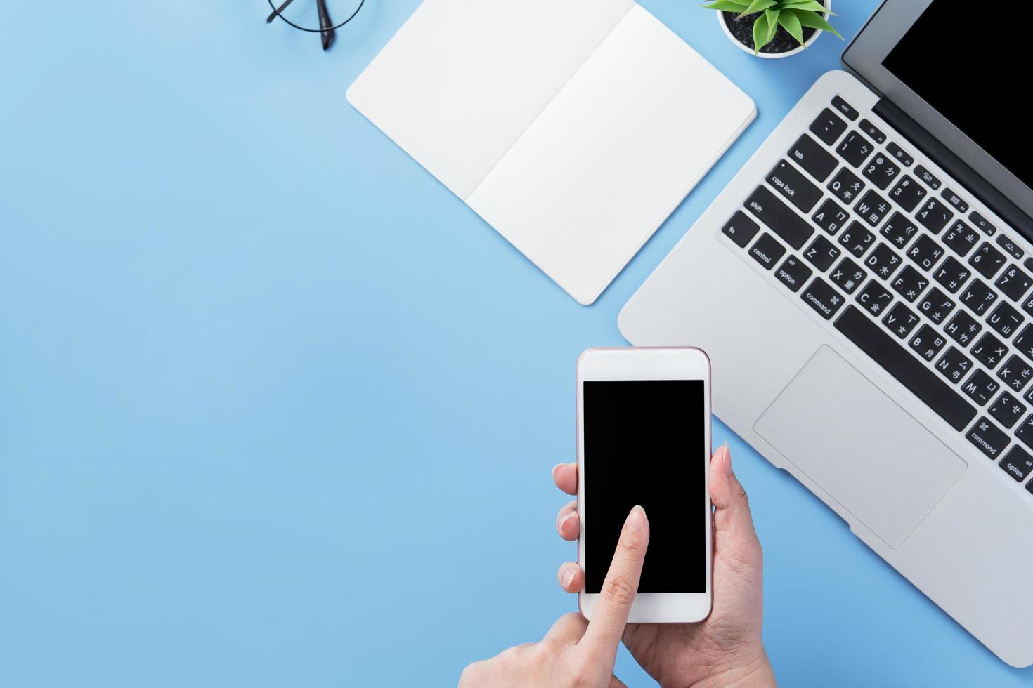 Woman holding smartphone with a minimal blue desk, concept of online shopping, internet payment, e-commerce, copy space, flat lay, top view, mock up photo