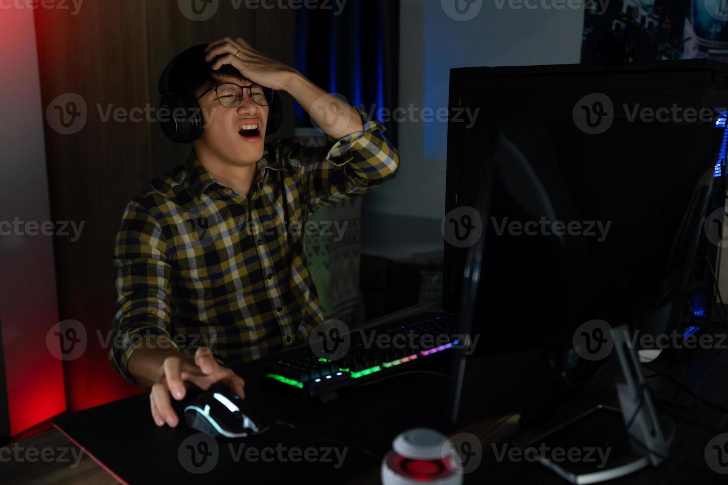 el jugador asiático con auriculares estresado con la mano se siente deprimido o enojado cuando pierde el videojuego en la computadora miedo y malestar por error, tecnología de videojuegos y concepto de deporte electrónico foto