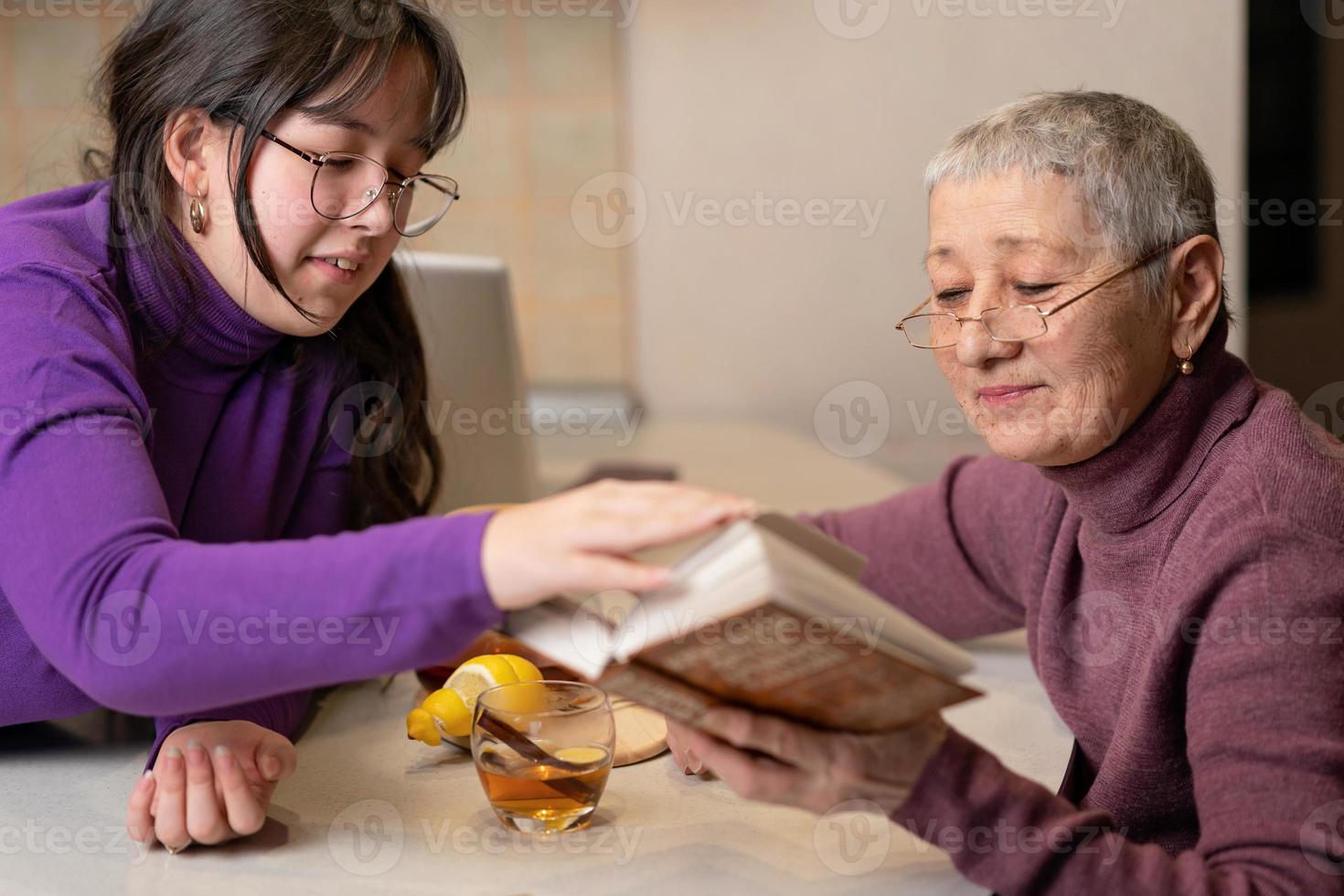 abuela y nieta beben té sentadas en la mesa y leen un libro. foto