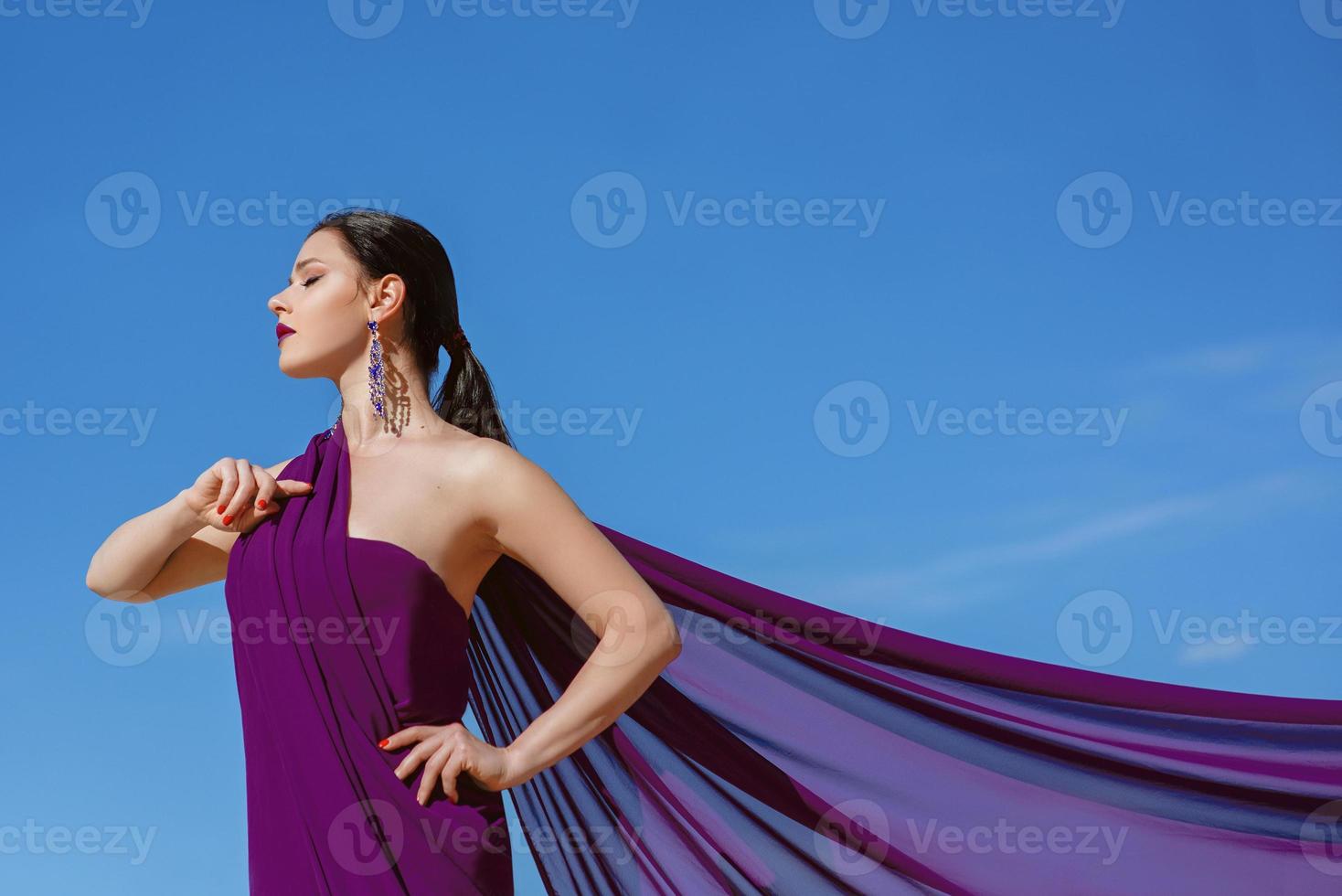 increíble hermosa mujer morena con la pluma de pavo real en tela púrpura en el desierto. oriental, indio, moda, concepto de estilo foto