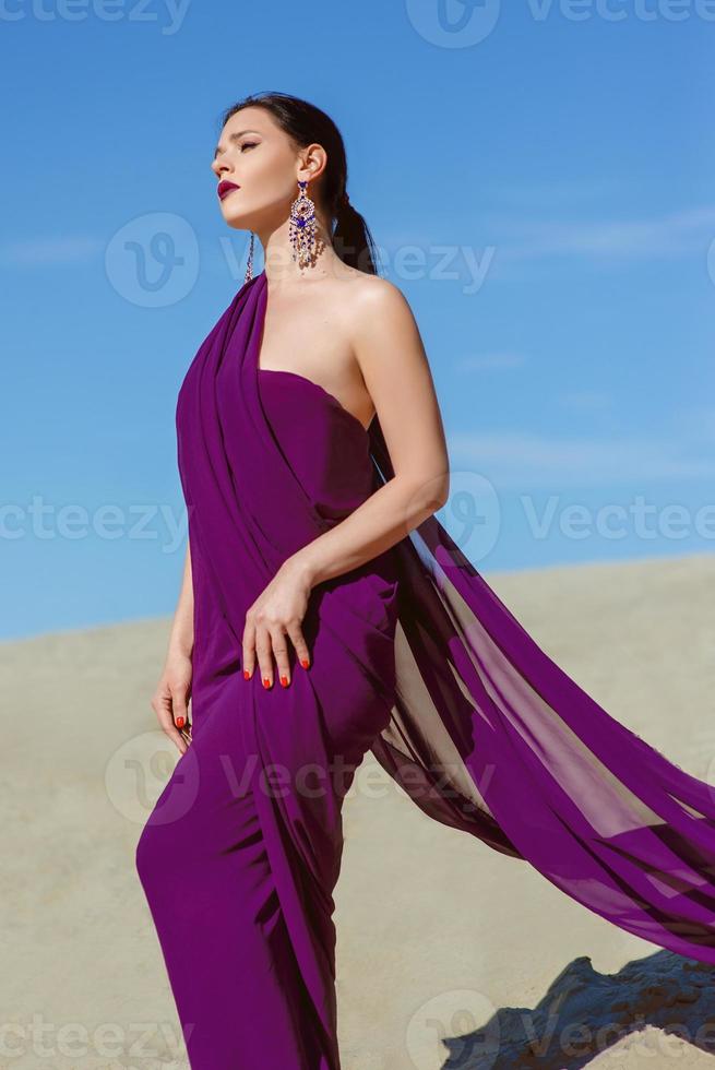 increíble hermosa mujer morena con la pluma de pavo real en tela púrpura en el desierto. oriental, indio, moda, concepto de estilo foto