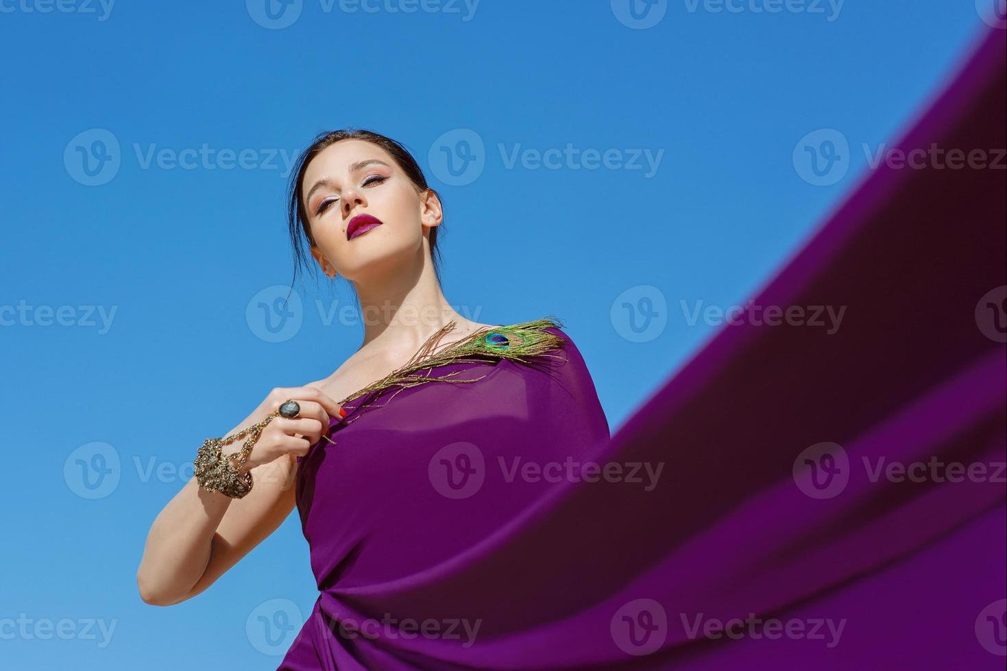 Amazing beautiful brunette woman with the Peacock feather in purple fabric in the desert. Oriental, indian, fashion, style concept photo