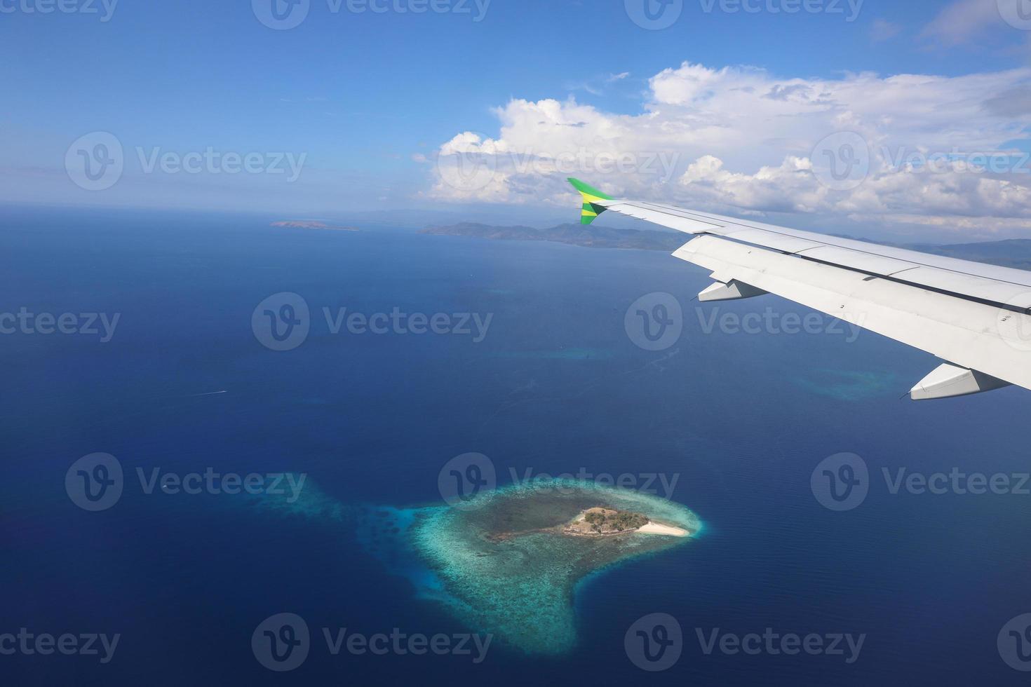 Airplane flying over deep blue sea with an island photo through window plane