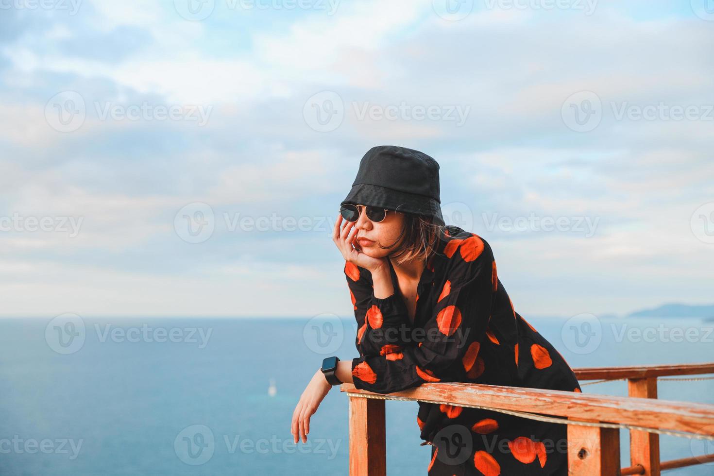 Asian woman in bucket hat and sunglasses enjoying ocean view from balcony photo