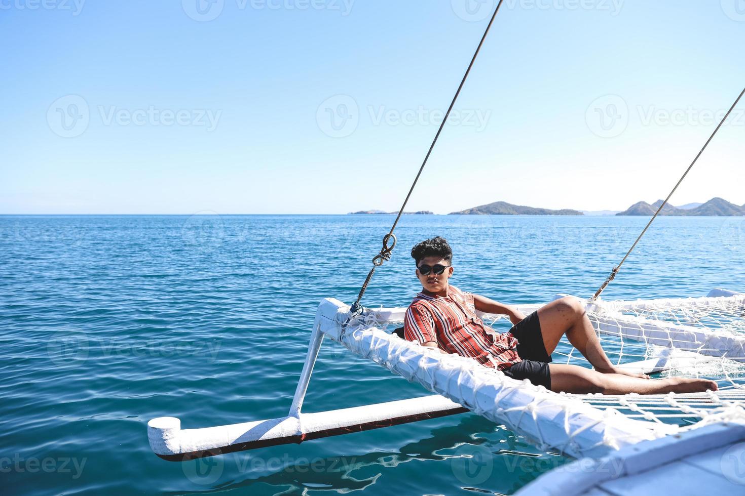 Asian man wearing sunglasses relaxing on catamaran net enjoying summer time photo