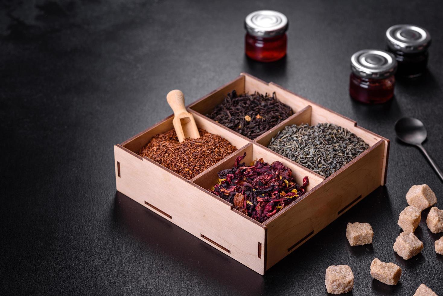 Several kinds of dry black tea with bergamot, rooibos, green and frame in a wooden box on a black concrete background photo