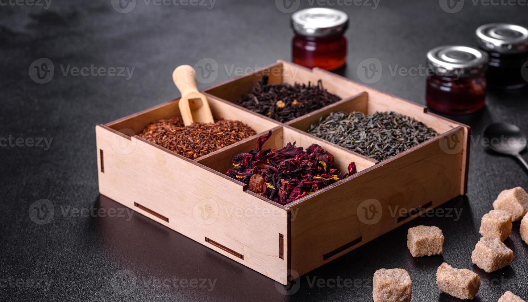 Several kinds of dry black tea with bergamot, rooibos, green and frame in a wooden box on a black concrete background photo