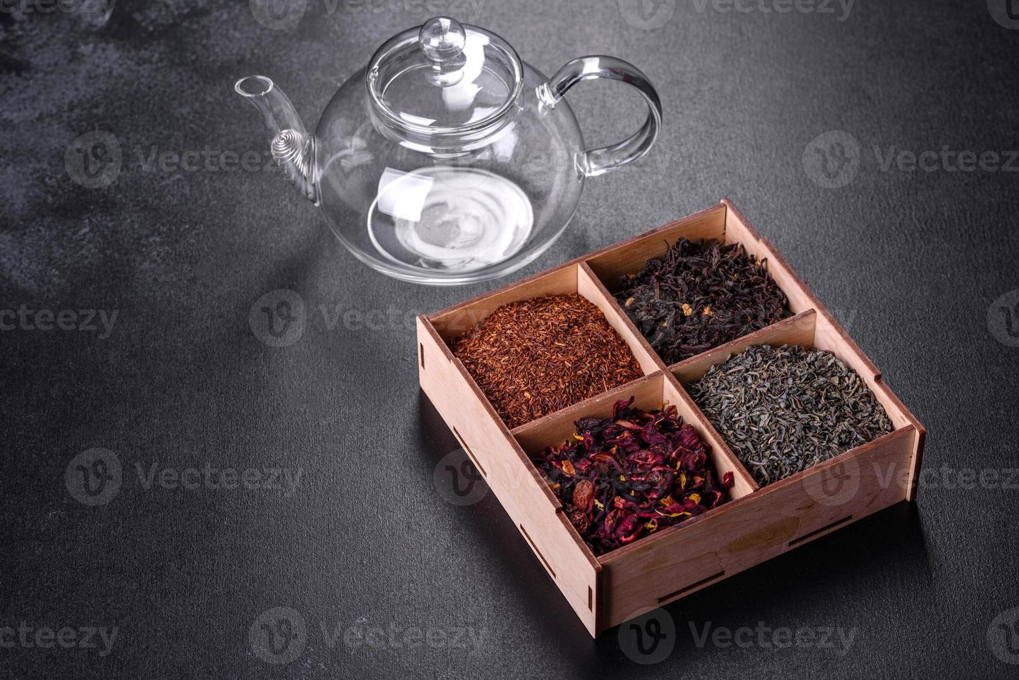 Several kinds of dry black tea with bergamot, rooibos, green and frame in a wooden box on a black concrete background photo