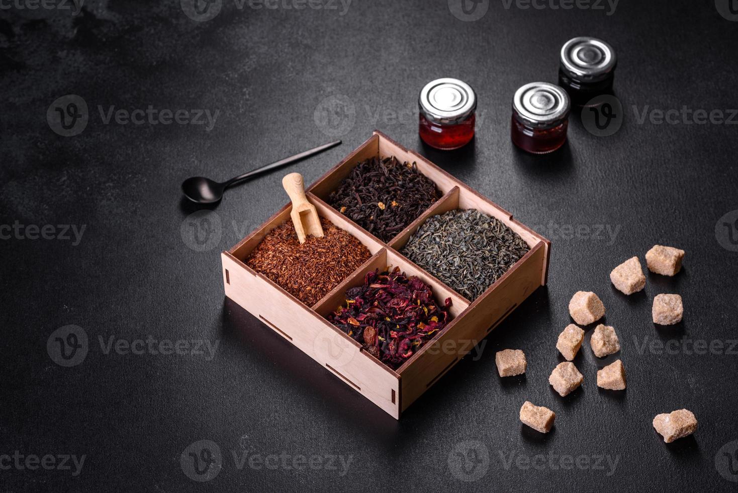 Several kinds of dry black tea with bergamot, rooibos, green and frame in a wooden box on a black concrete background photo