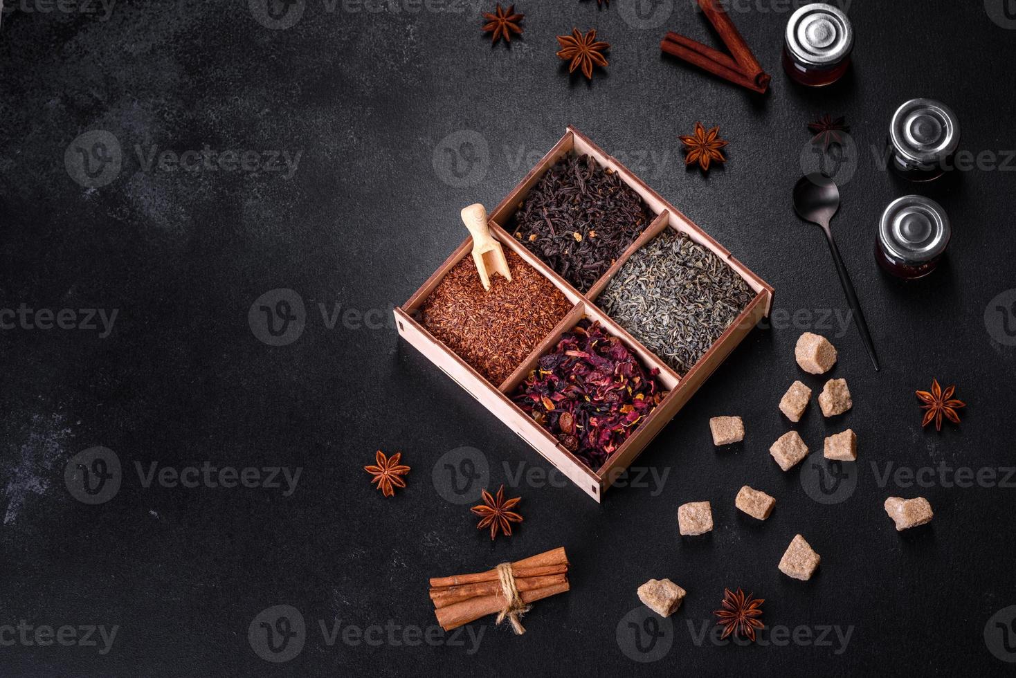 Several kinds of dry black tea with bergamot, rooibos, green and frame in a wooden box on a black concrete background photo