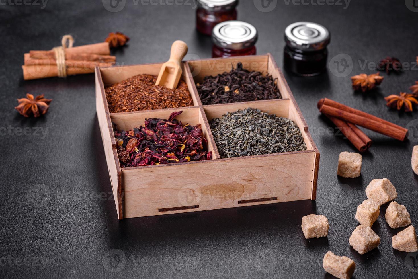 varios tipos de té negro seco con bergamota, rooibos, verde y marco en una caja de madera sobre un fondo de hormigón negro foto