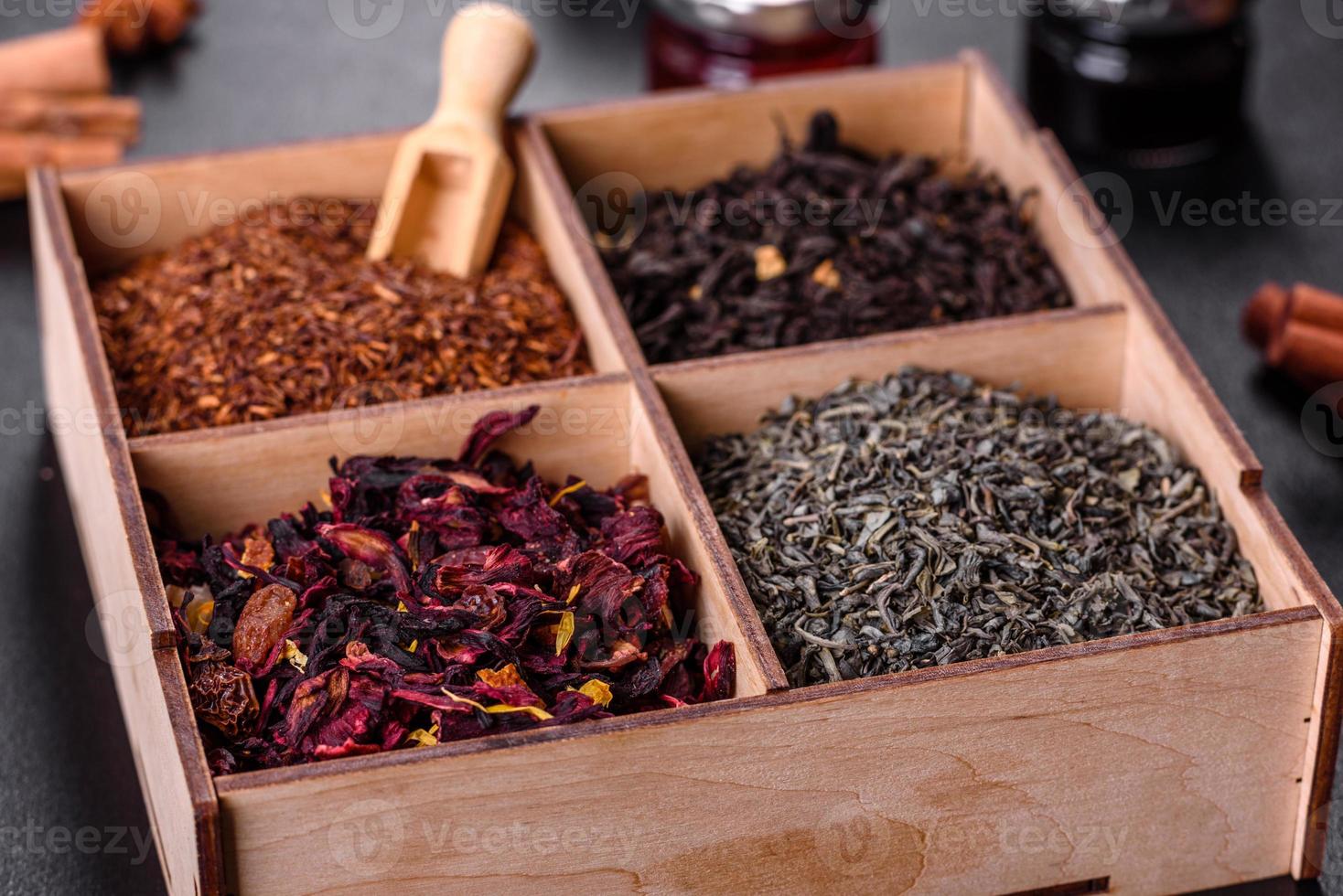 Several kinds of dry black tea with bergamot, rooibos, green and frame in a wooden box on a black concrete background photo