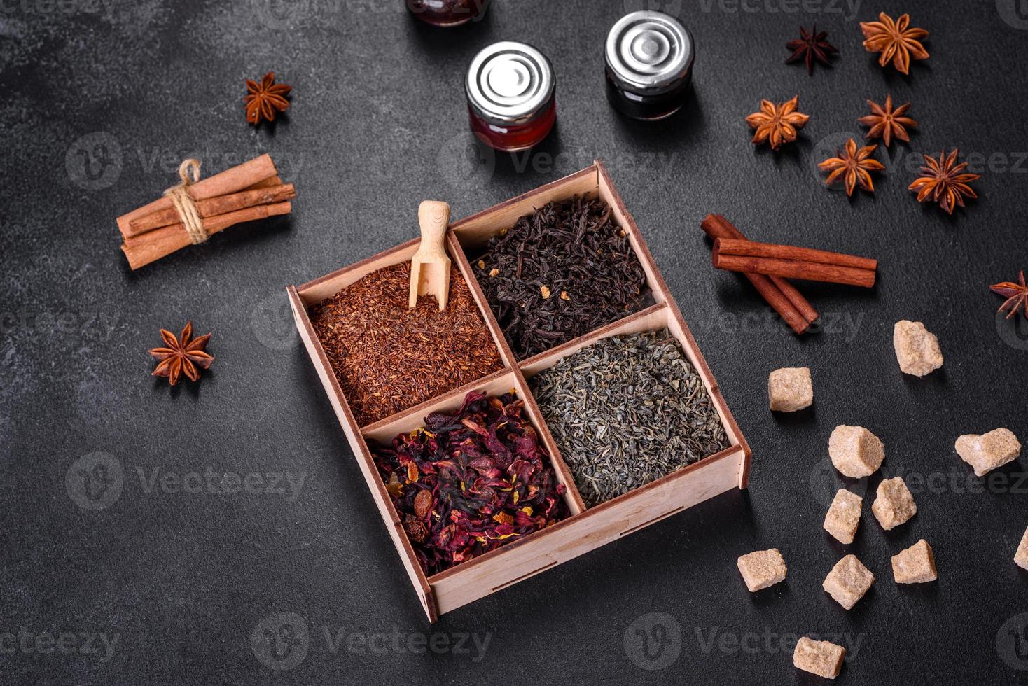 Several kinds of dry black tea with bergamot, rooibos, green and frame in a wooden box on a black concrete background photo