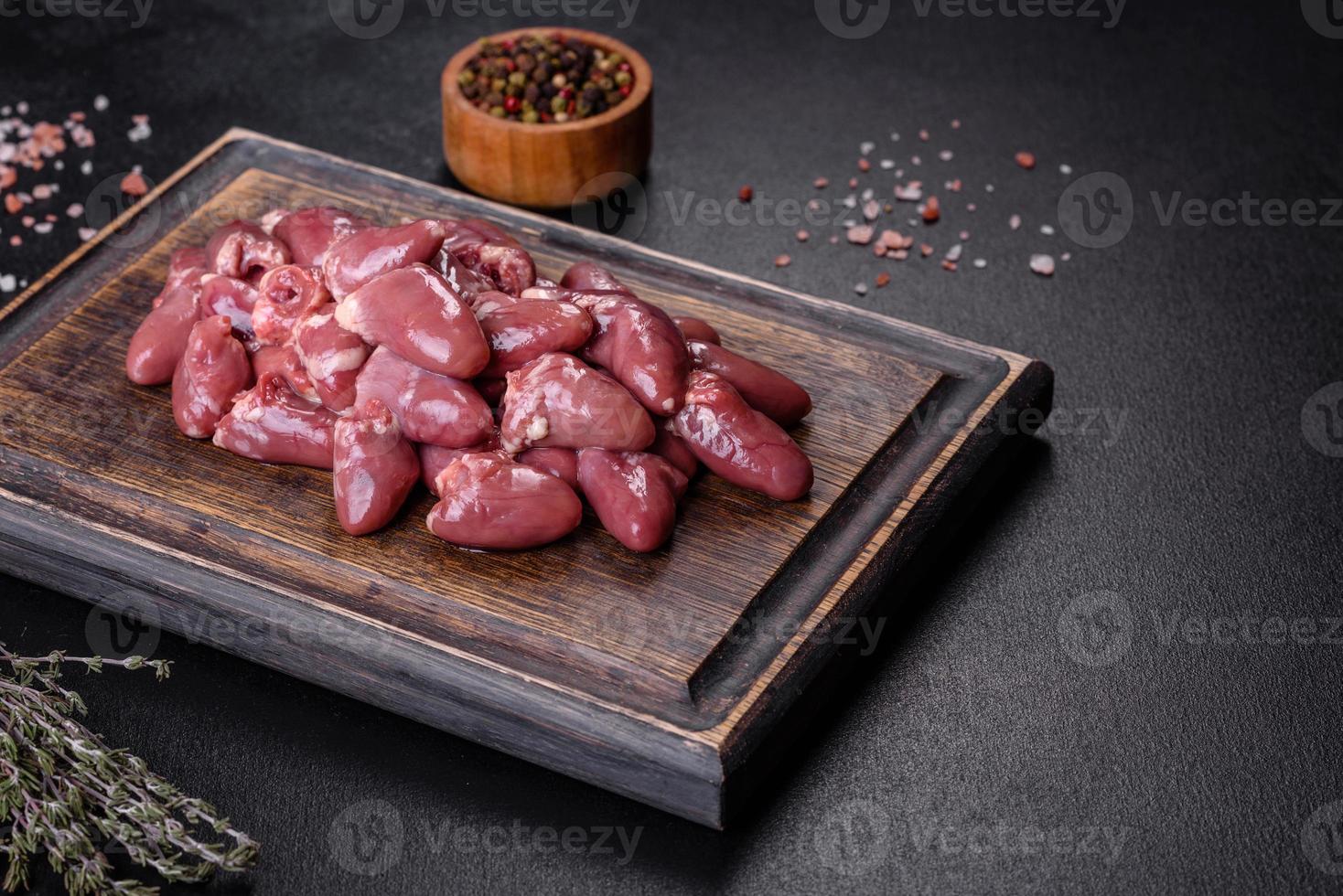 Raw uncooked chicken hearts on wooden cutting board on a dark concrete table photo