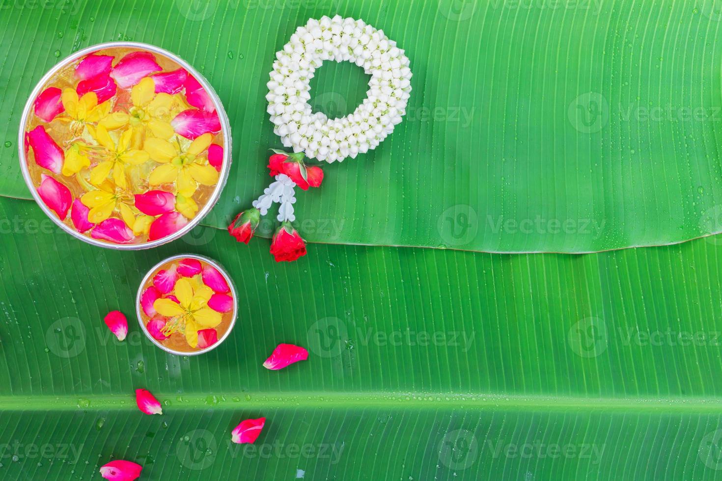 Songkran Festival background with jasmine garland Flowers in a bowl of water, perfume and limestone on a green wet banana leaf background. photo