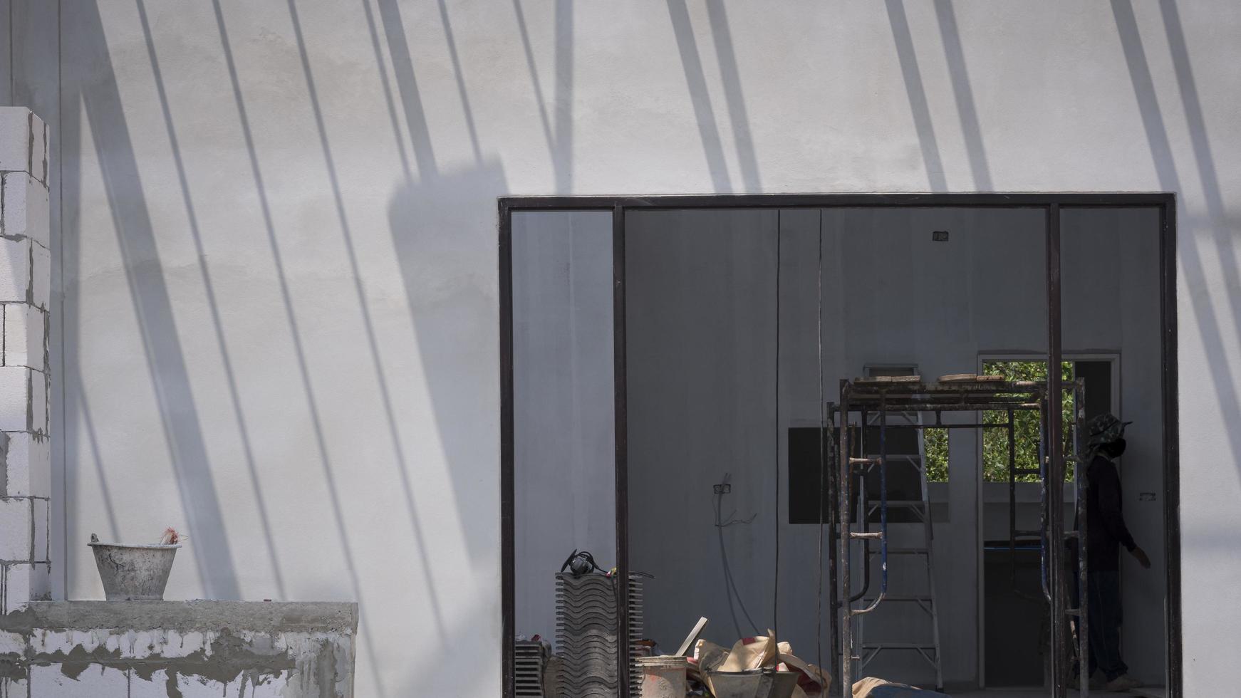 luz solar y sombra en la superficie de la pared de hormigón con material de construcción y equipo en el marco de la puerta dentro del sitio de construcción de la casa foto