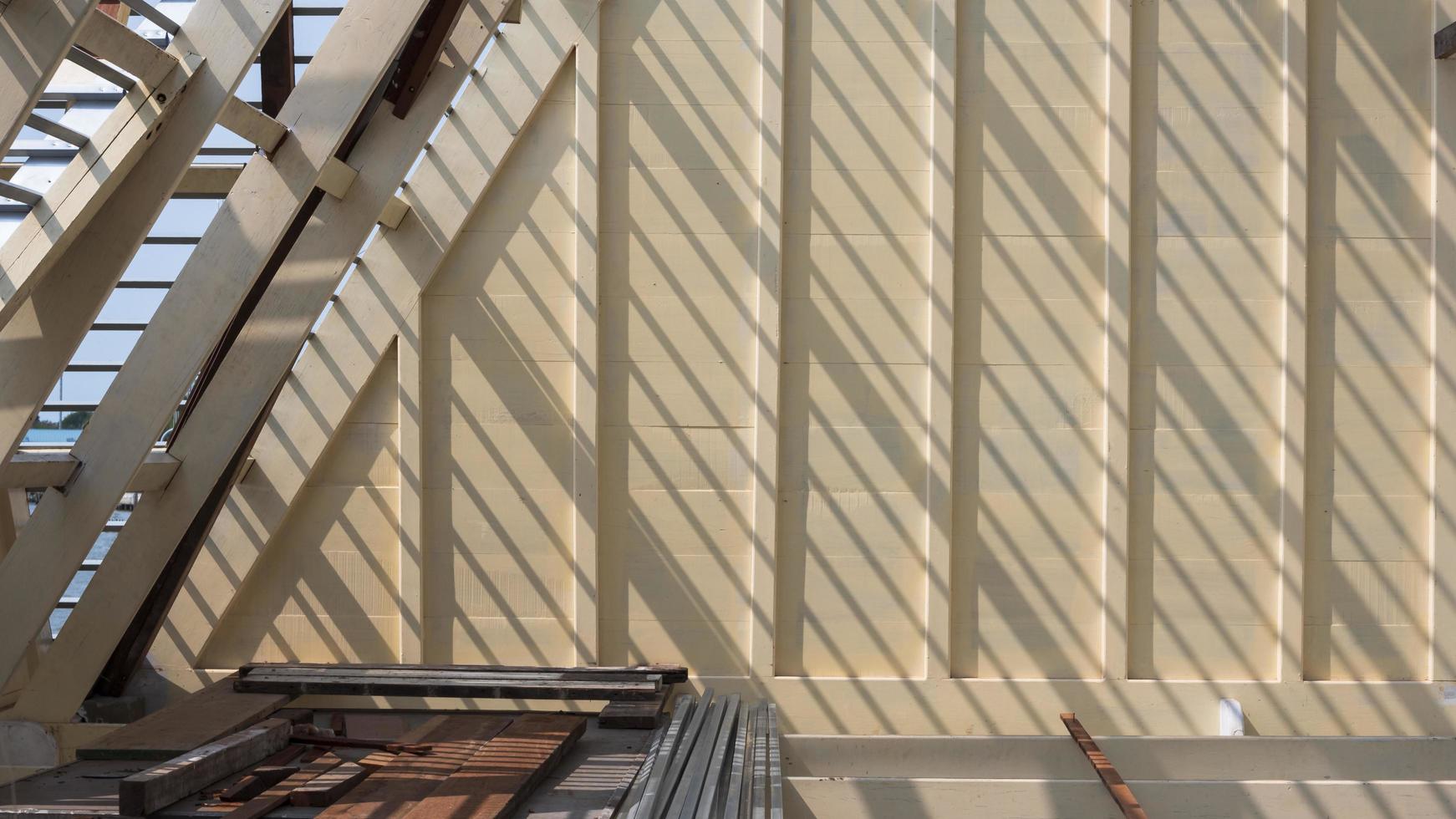 Sunlight and shadow on surface of white wooden roof truss structure with construction material on top of house building site photo